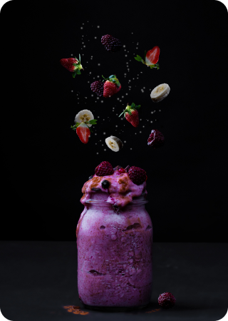 a bowl with milkshake and fruit falling inside the bowl too